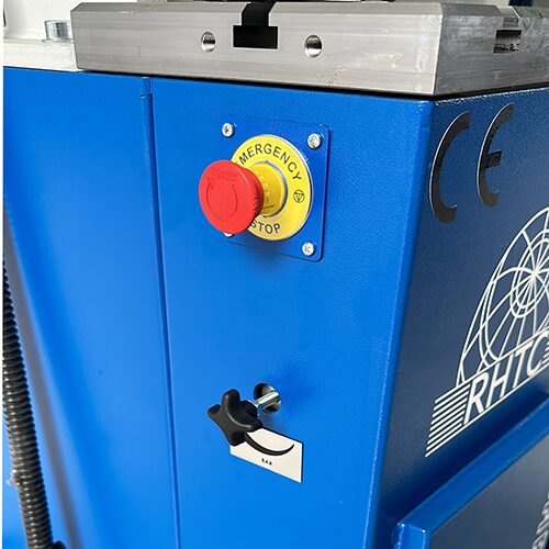 Side view of a punching press with emergency stop and pressure adjustment. The press is a large, heavy-duty machine with a long, cylindrical ram. The ram is connected to a control panel at the top of the machine. The control panel has a red emergency stop button and a pressure adjustment knob.