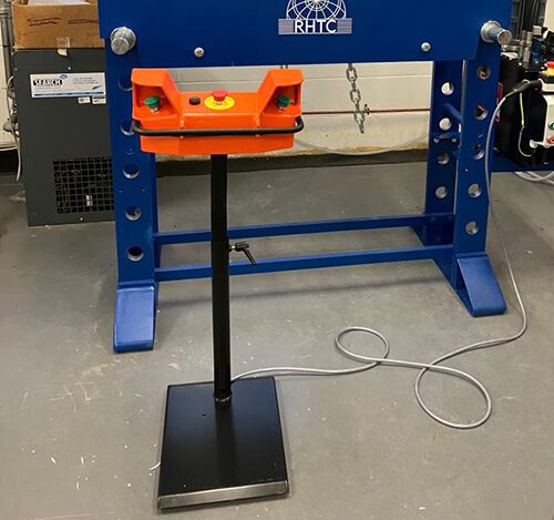 Close-up of hydraulic workshop press with ergonomic two-hand button controls, emphasizing safety and precision in metal fabrication.